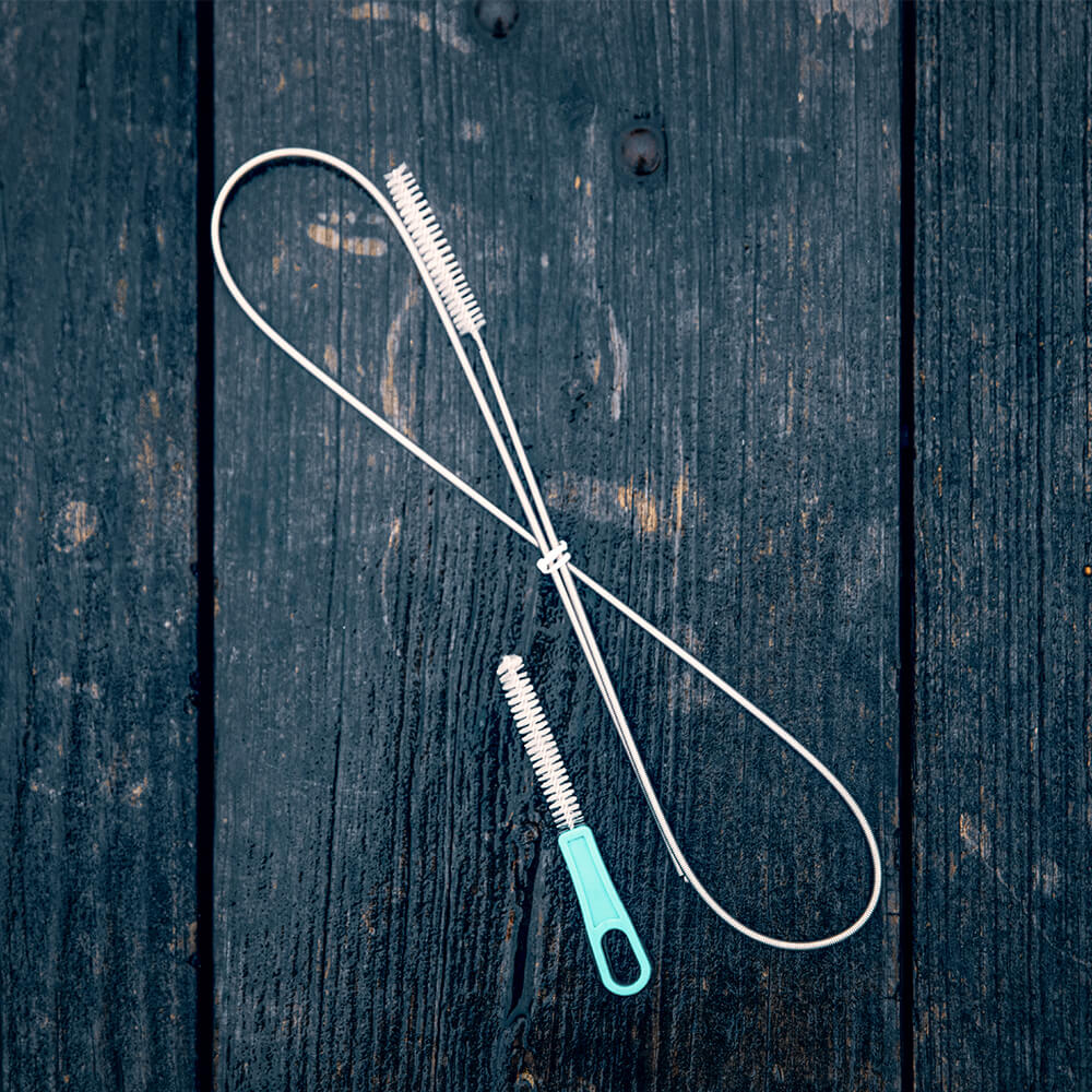 A bite valve brush and hose brush for Vayska cleaning kits sits on a damp piece of wood. Each kit will come with two of each kind of brush.