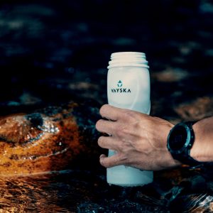 Someone filling a Vayska water bottle from a cold mountain river. The water probably feels amazing, but drinking unfiltered water might be dangerous, so don't do it. NOOOOO.